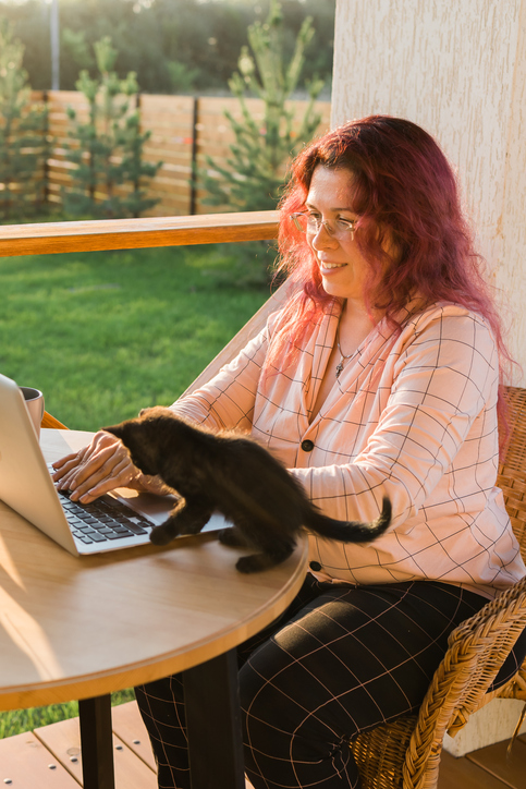 Woman completing paperwork while a curious kitten explores the laptop.